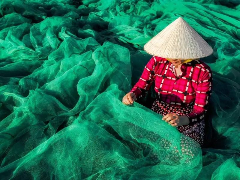 Locals wearing non la while making fishing nets in Vietnam